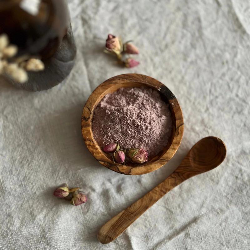 Natural pink clay face mask powder in a wooden bowl with dried rosebuds – botanical skincare for sensitive skin and self-care rituals UK.