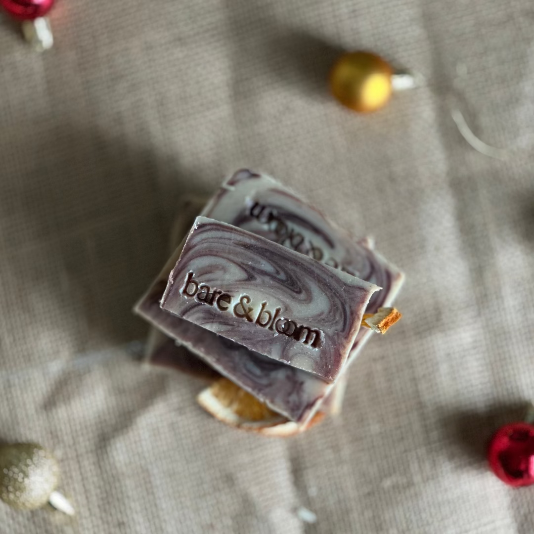 seasonal bar of soap with 'bare & bloom' branding on a textured surface with Christmas ornaments.