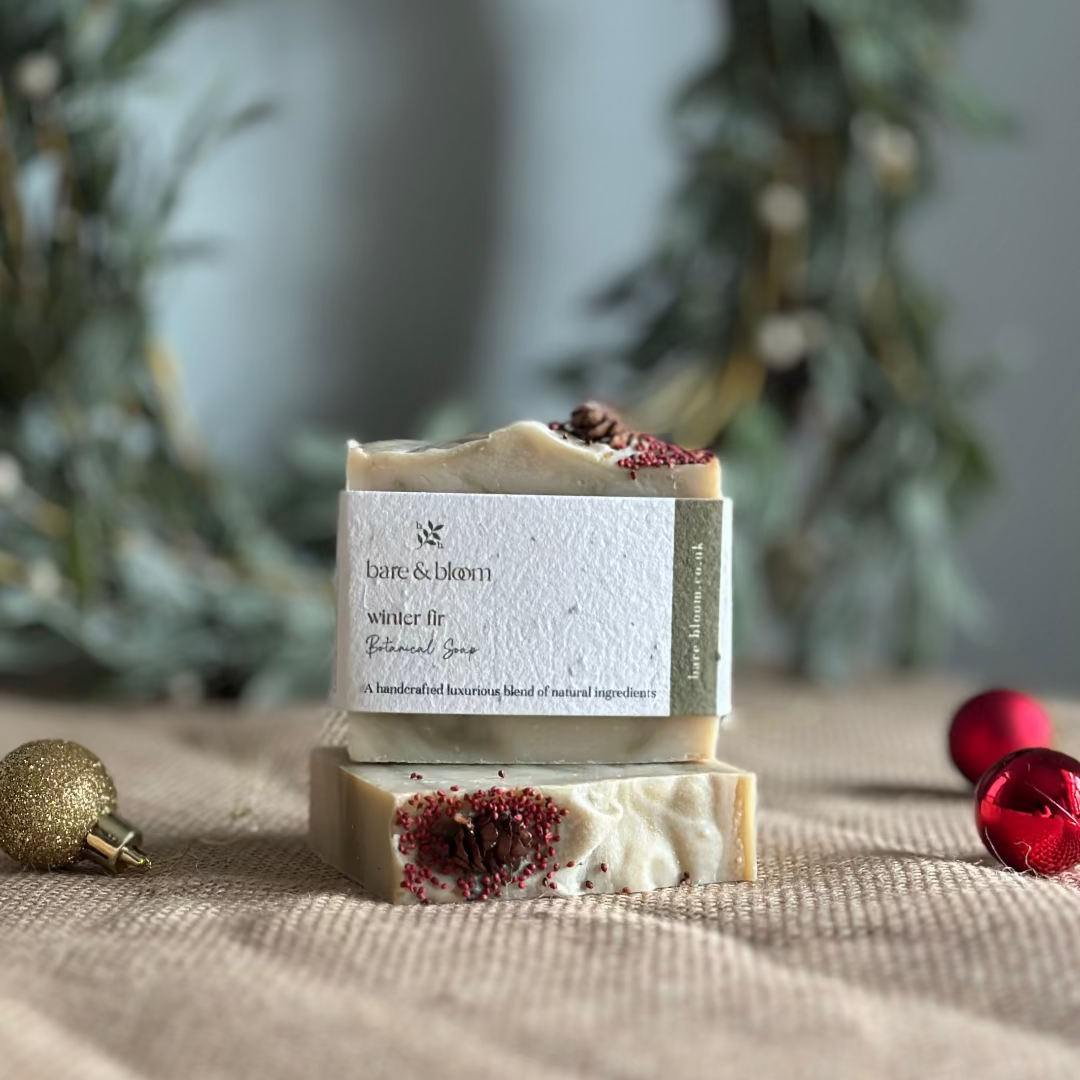 Two bars of soap with a visible bare and bloom label on a textured surface with Christmas decorations.
