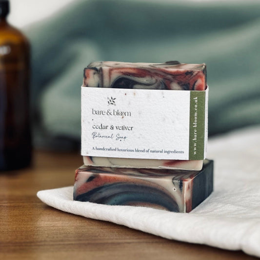 artisan soap wrapped with seeded label on white cloth and amber jar  in background